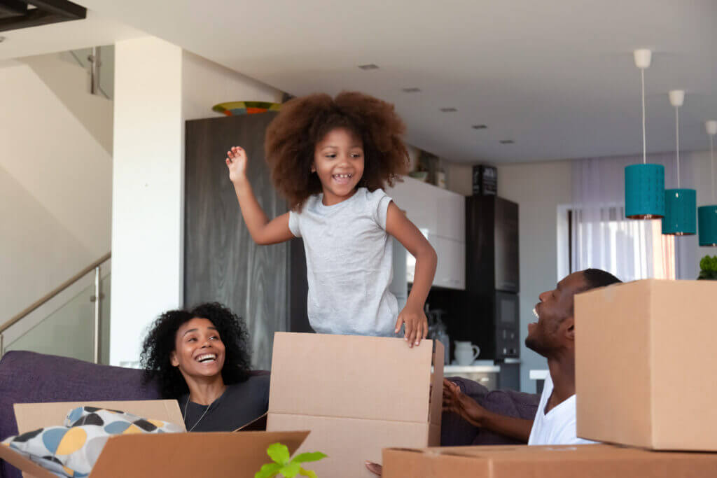 Happy African American child and parents unpacking boxes in new house